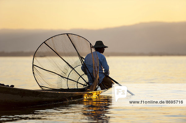 Fisherman in the evening light  with a traditional basket  sitting on a canoe  sunset at Inle Lake  Shan State  Myanmar