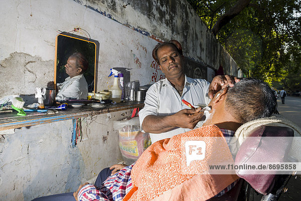 Ein Barbier rasiert einen Kunden in seinem Freiluft-Laden  Ahmedabad  Gujarat  Indien