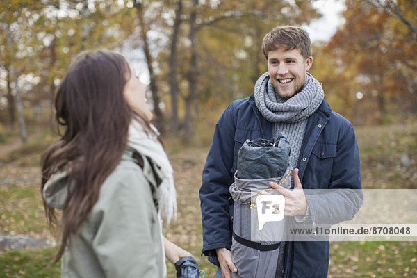 Happy man in winter jacket and scarf looking at woman during camping
