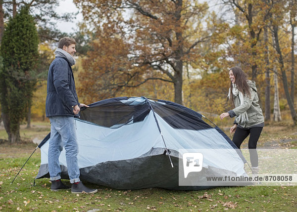Full length of young couple pitching tent in forest