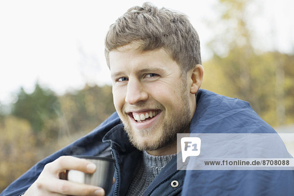 Portrait of happy man wrapped in blanket holding coffee cup