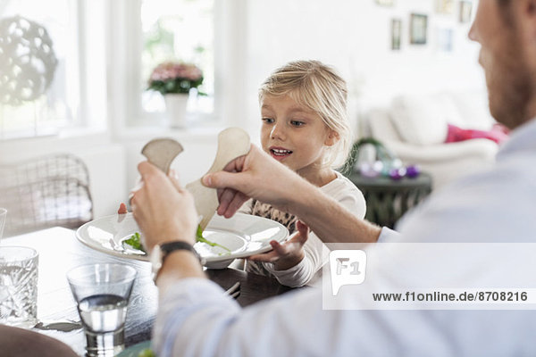 Father serving salad to daughter at dining table
