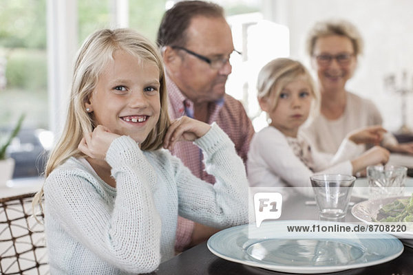 Porträt eines glücklichen Mädchens,  das mit seiner Familie am Esstisch sitzt.