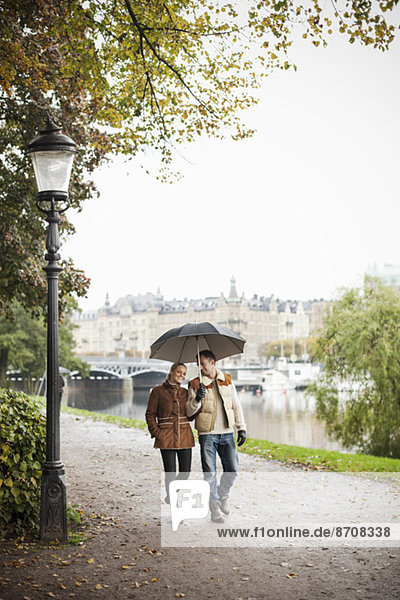 Junges Paar mit Regenschirm auf der Straße im Herbst