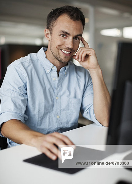 Porträt eines lächelnden Geschäftsmannes mit Computer im Büro