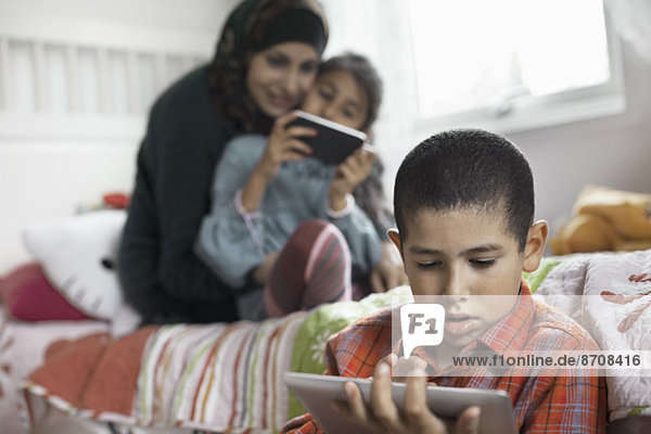 Boy using digital tablet in bedroom with family in background