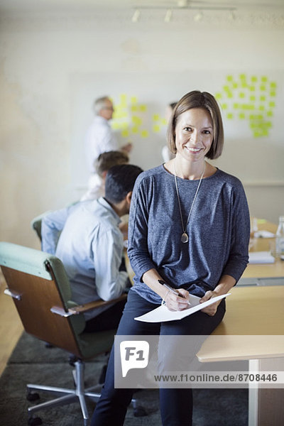 Portrait of confident businesswoman in conference room with colleagues discussing in background