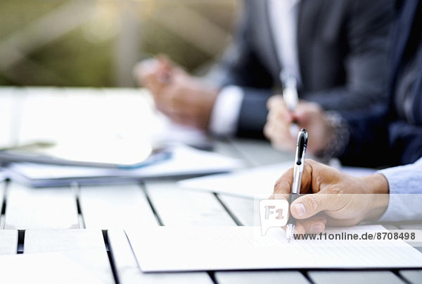 Abgeschnittenes Bild eines Geschäftsmannes  der auf einem Dokument am Tisch schreibt.