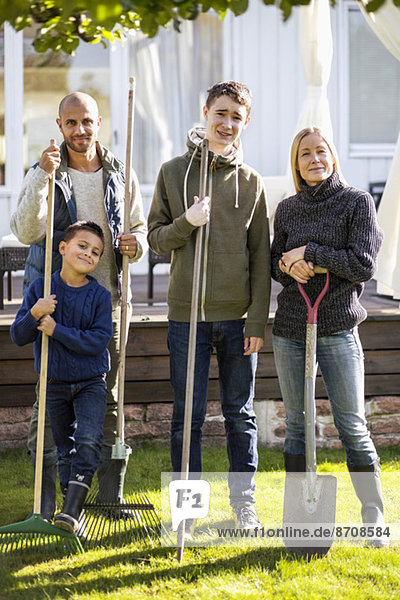 Portrait of confident family with gardening equipment standing at yard