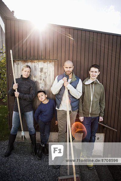 Porträt einer selbstbewussten Familie mit Gartengeräten am Haus
