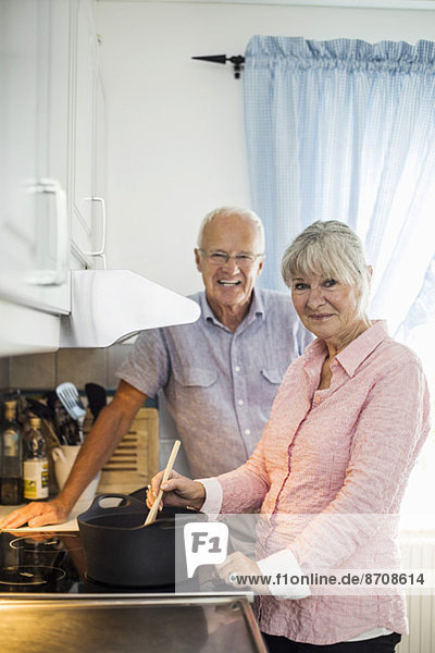 Porträt eines glücklichen Seniorenpaares beim Kochen am Küchentisch