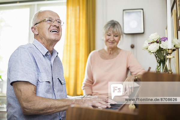 Glücklicher älterer Mann,  der Klavier spielt,  während er mit einer Frau im Haus sitzt.