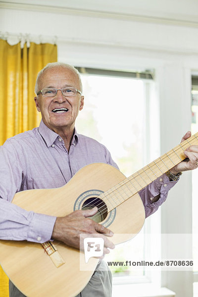 Porträt eines glücklichen Mannes  der zu Hause Gitarre spielt