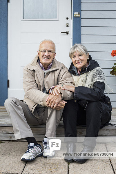 Porträt eines lächelnden älteren Paares  das auf der Veranda sitzt.