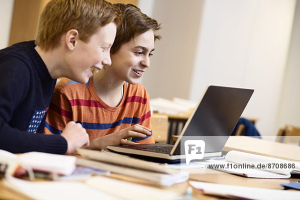 Schoolboys using laptop together in classroom