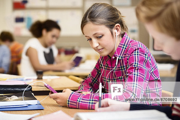 Schoolgirl listening music through smart phone in classroom