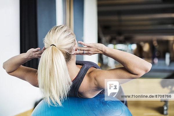 Junge Frau beim Training auf dem Fitnessball im Fitnessstudio
