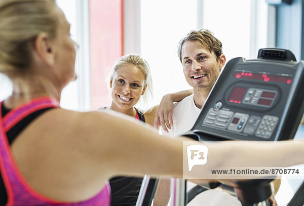Friends looking at woman exercising on treadmill at gym
