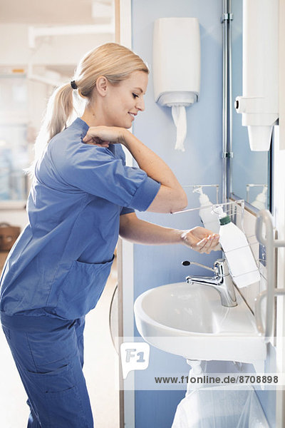 Seitenansicht der jungen Krankenschwester mit Seifenspender zum Händewaschen im Bad