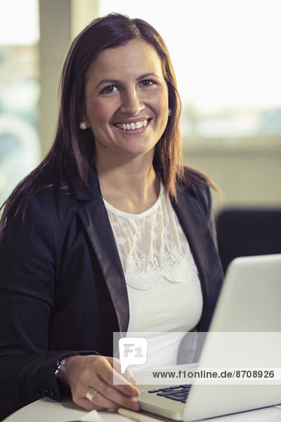 Porträt einer lächelnden Geschäftsfrau sitzend mit Laptop am Schreibtisch
