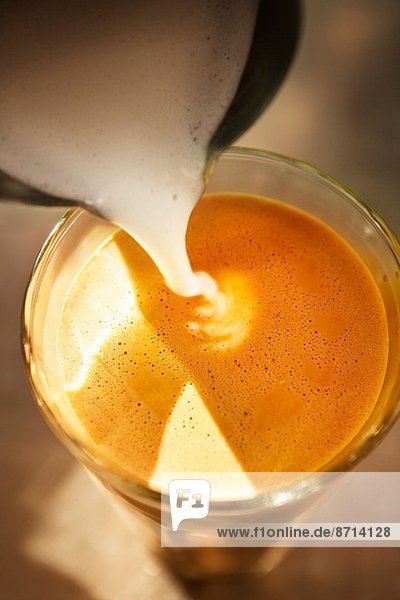 Nahaufnahme von aufgeschäumter Milch  die in ein Kaffeeglas gegossen wird.