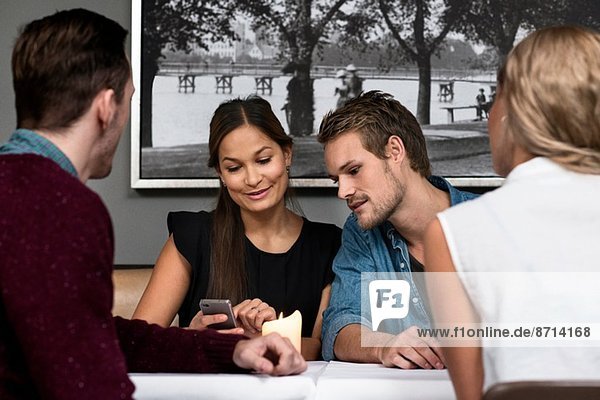 Vier junge erwachsene Freunde sitzen im Cafe und schauen auf das Handy