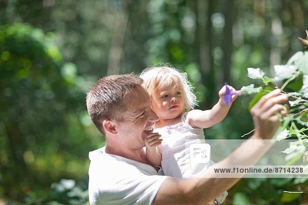 Father with baby girl plucking flowers in forest