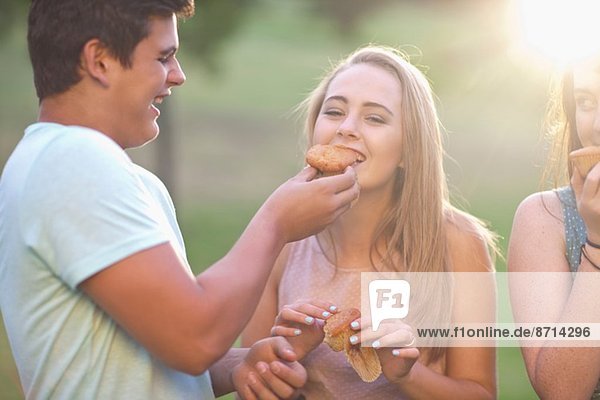 Junge fütterndes Mädchen  Freund im Hintergrund