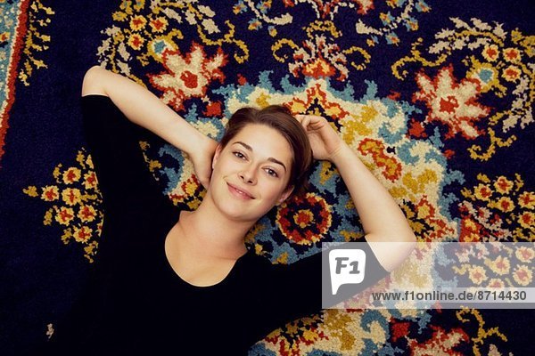 Portrait einer jungen Frau auf gemustertem Teppich liegend