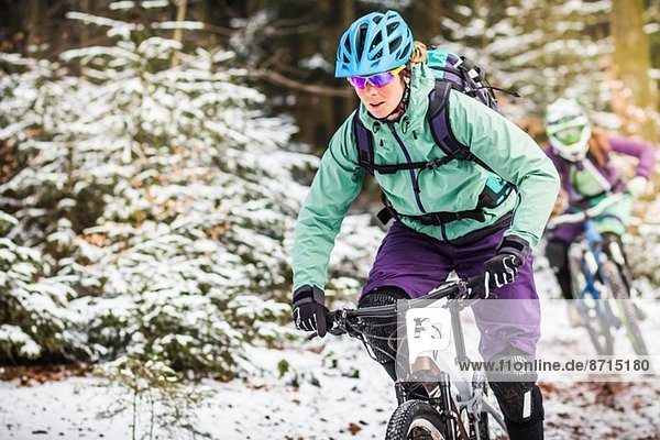 Two female mountain bikers riding through forest in snow