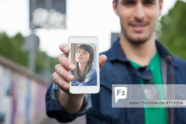 Junger Mann hält Smartphone mit Foto der Freundin in der Hand