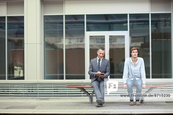 Businessman and young man sitting on train station bench