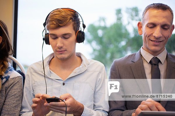 Junger Mann hört Kopfhörer und benutzt Smartphone im Zug