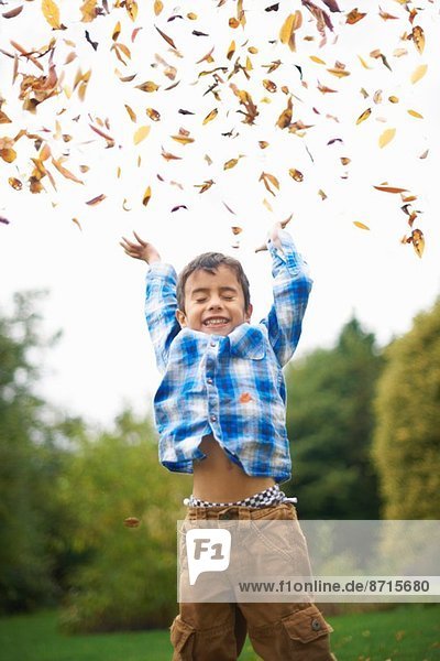 Male toddler in the garden throwing up autumn leaves