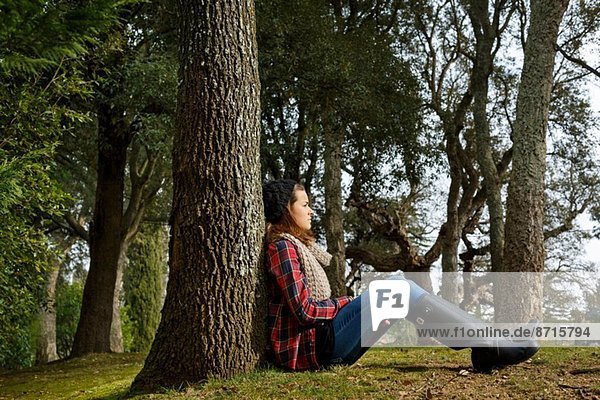 Teenager-Mädchen am Baum im Wald sitzend