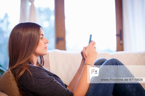 Junge Frau mit Handy auf dem Sofa