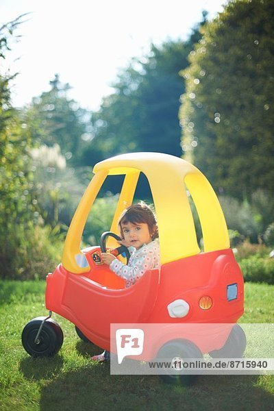 Kleinkind beim Spielen im Spielzeugauto im Garten
