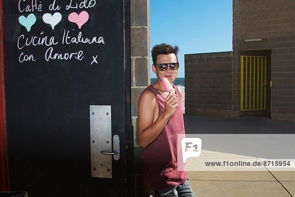 Young man enjoying ice lolly outside ice cream parlour