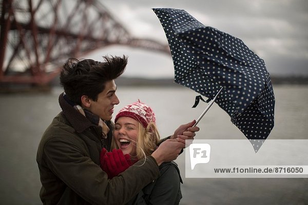 Ein junges Paar kämpft mit einem Regenschirm vor der Forth Rail Bridge in Queensferry  nahe Edinburgh  Schottland.