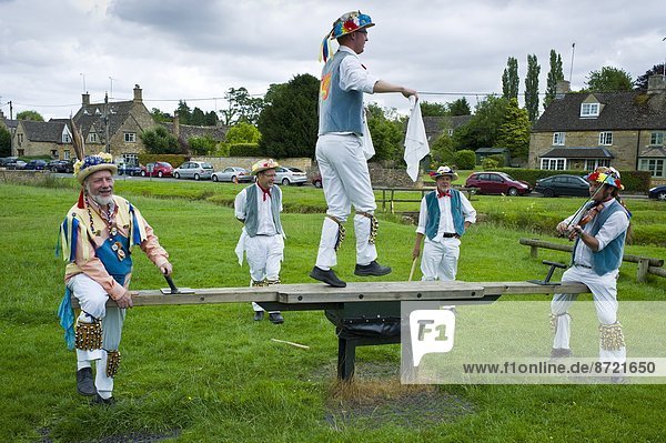 Morris dancers  Icknield Way Morris Men  in children's playground at The Kings Head Pub  Bledington  Oxfordshire  UK