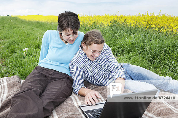 Young couple in front of a laptop on a meadow