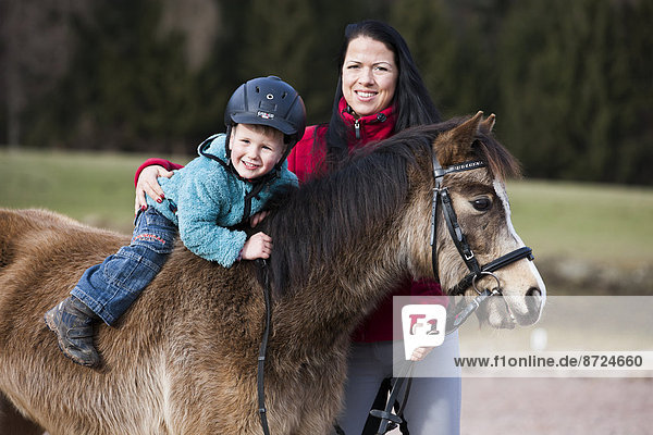 Kleines Kind mit Helm sitzt ohne Sattel auf einem Pony  Falbe  mit Trense  mit Reitlehrerin Tirol  Österreich