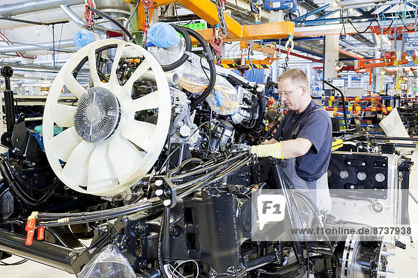 Mitarbeiter beim Einbau von Motor und Getriebe in das Fahrgestell bei der MAN Truck und Bus AG München Oberbayern Bayern Deutschland