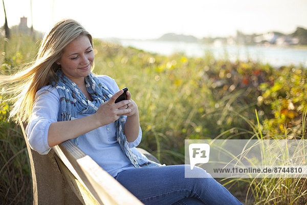 Young Woman Sitting on Bench at Beach  Texting on Cell Phone  Jupiter  Palm Beach County  Florida  USA