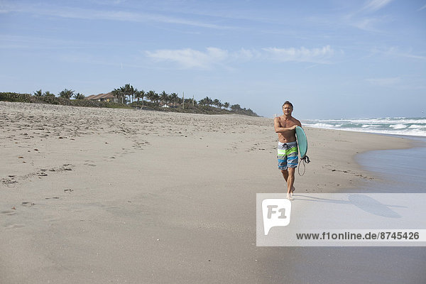Mature Man Walking down Beach with Surfboard  USA