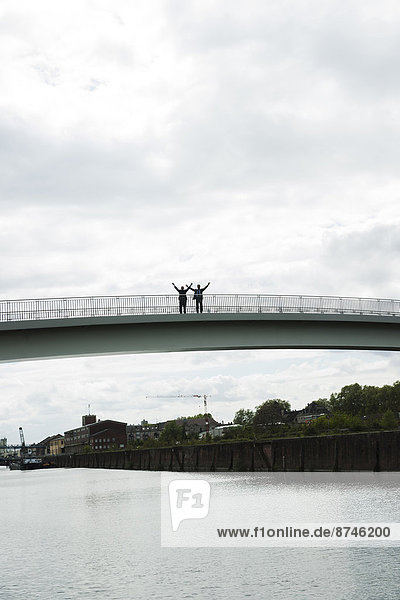 Silhouette of mature businessmen standing on bridge with arms in air  Mannheim  Germany
