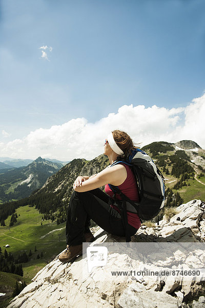 Mature woman sitting on cliff  hiking in mountains  Tannheim Valley  Austria