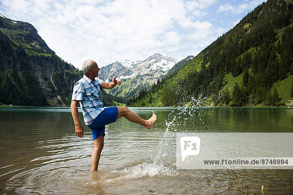 Mature man standing in lake  kicking water  Lake Vilsalpsee  Tannheim Valley  Austria