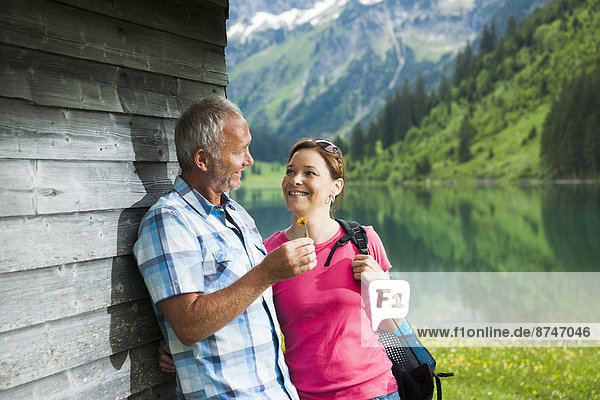 Mature man offering flower to mature woman  standing next to building at Lake Vilsalpsee  Tannheim Valley  Austria