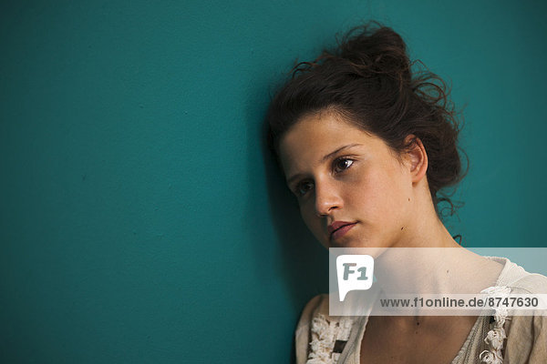 Portrait of teenaged girl  leaning against wall  looking off into the distance